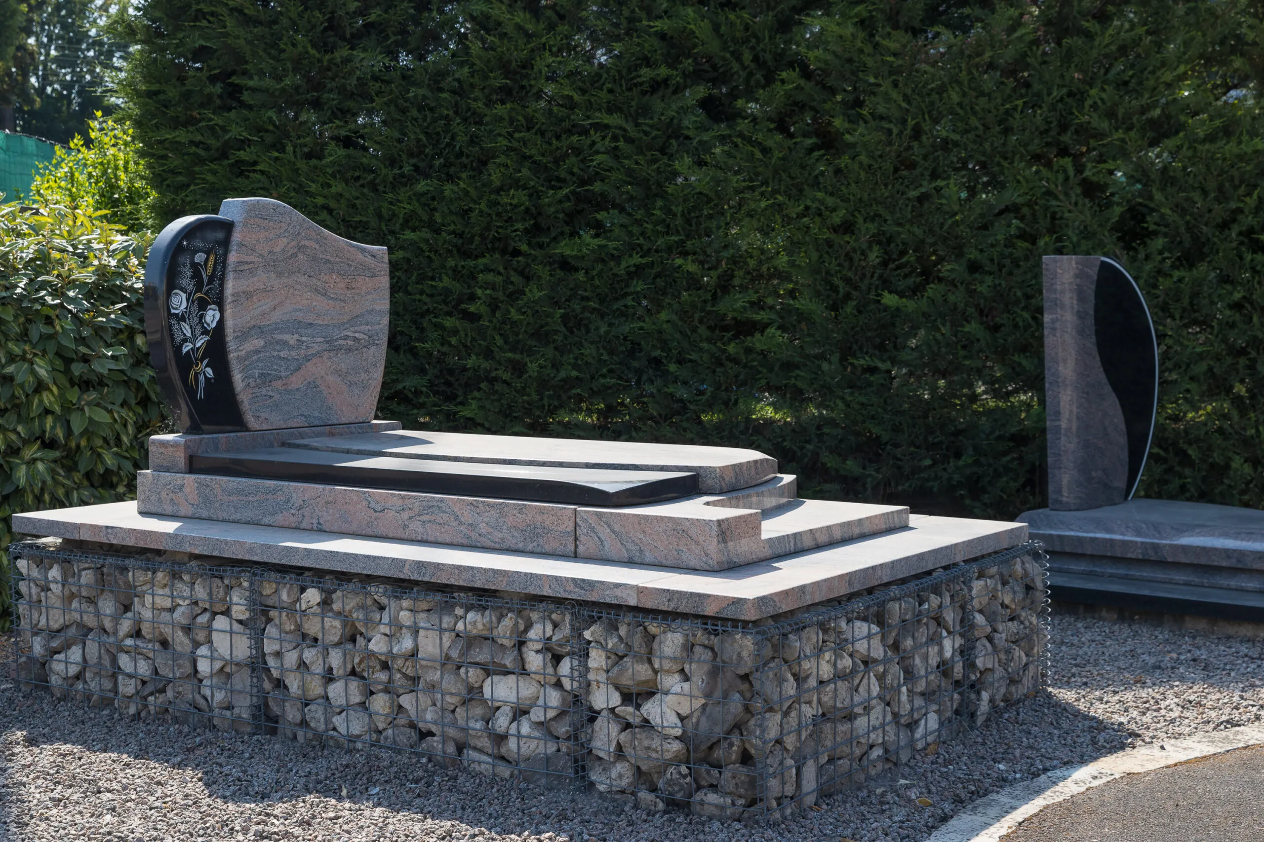 Pierre tombale en granit rose et noir exposée sur un socle en gabion